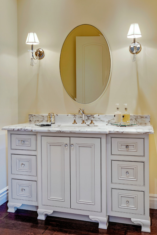 Ispirazione per un piccolo bagno di servizio classico con ante a filo, ante bianche, top in marmo, piastrelle bianche, pareti gialle, parquet scuro e lavabo sottopiano