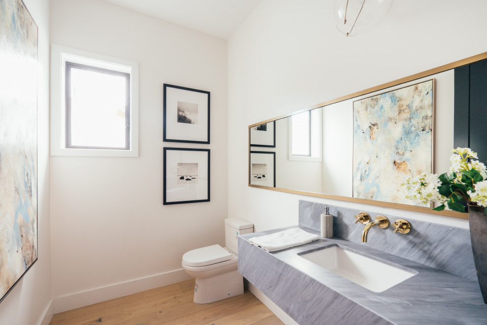 ロサンゼルスにあるビーチスタイルのおしゃれなトイレ・洗面所 (白い壁、無垢フローリング、アンダーカウンター洗面器、茶色い床、グレーの洗面カウンター、三角天井) の写真