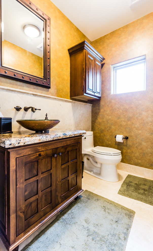 Powder room - small mediterranean beige tile and porcelain tile travertine floor powder room idea in Austin with a vessel sink, furniture-like cabinets, dark wood cabinets, granite countertops and a one-piece toilet