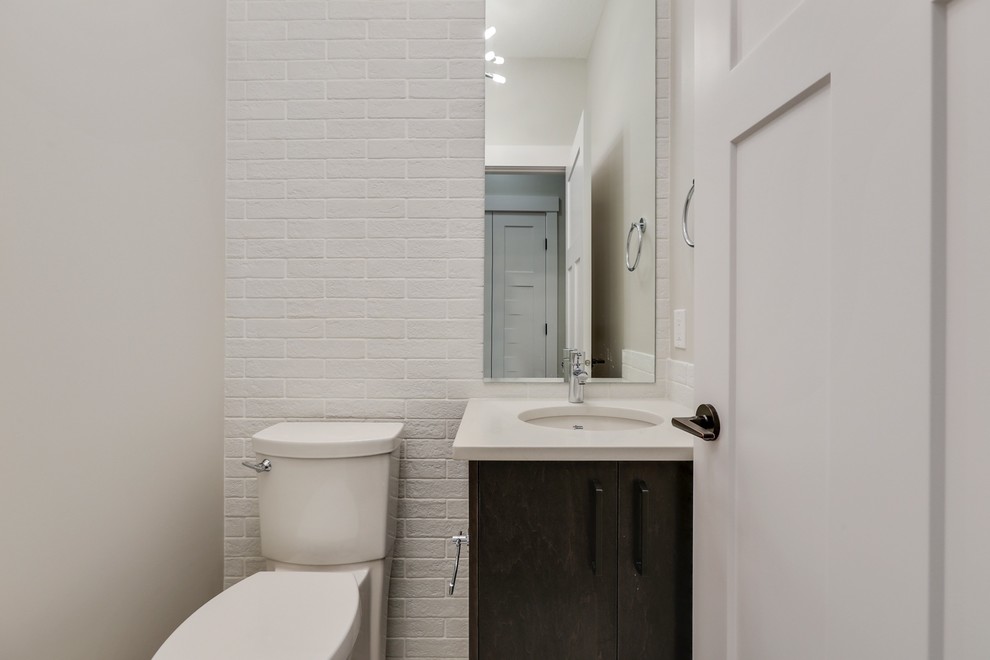 На фото: туалет в современном стиле с плоскими фасадами, унитазом-моноблоком, белой плиткой, белыми стенами, врезной раковиной, столешницей из искусственного кварца и темными деревянными фасадами с
