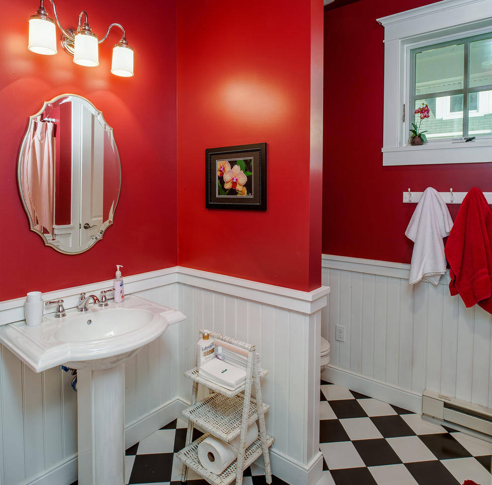 Bild på ett mellanstort amerikanskt toalett, med vita skåp, en toalettstol med hel cisternkåpa, röda väggar, ett piedestal handfat, laminatgolv och flerfärgat golv