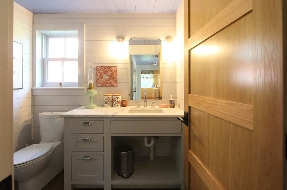 Réalisation d'un petit WC et toilettes champêtre avec un placard avec porte à panneau encastré, des portes de placard grises, un plan de toilette en marbre, un mur blanc, WC séparés, un lavabo encastré et un plan de toilette blanc.
