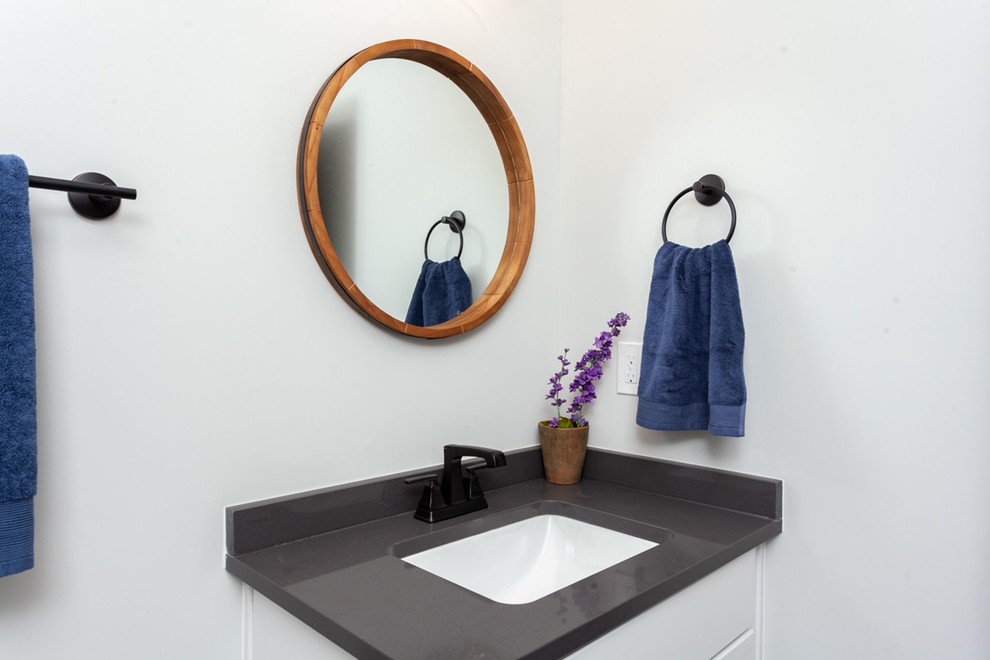 Esempio di un bagno di servizio american style di medie dimensioni con pareti bianche, lavabo sottopiano, top in superficie solida e top nero