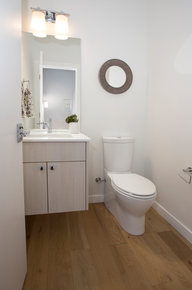 Cette photo montre un petit WC et toilettes moderne en bois clair avec un placard à porte plane, WC séparés, un mur blanc, un sol en bois brun, un lavabo encastré, un plan de toilette en quartz modifié et un sol marron.