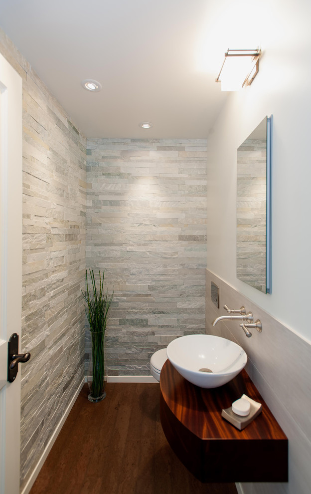 Aménagement d'un WC et toilettes moderne avec un carrelage gris, un carrelage de pierre, une vasque, un plan de toilette en bois et un sol marron.