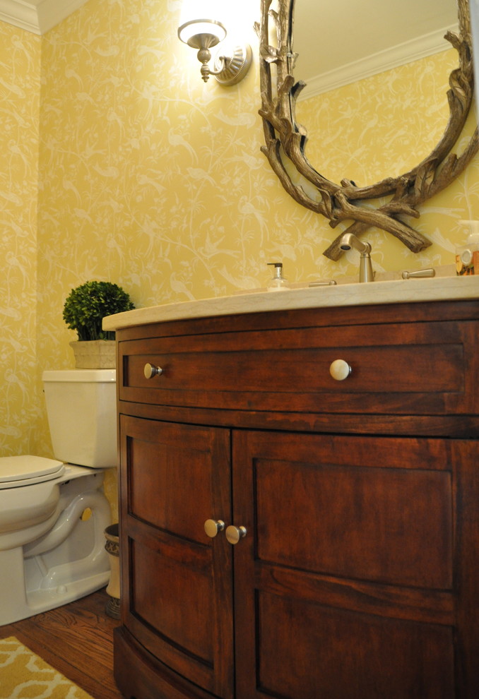 Idée de décoration pour un WC et toilettes tradition en bois brun de taille moyenne avec un placard avec porte à panneau encastré, un mur jaune, parquet foncé et un plan de toilette en marbre.