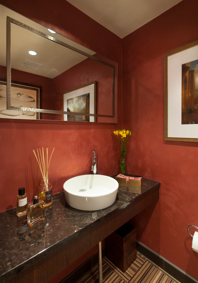 Modern inredning av ett litet toalett, med ett fristående handfat, skåp i mörkt trä, granitbänkskiva, en toalettstol med hel cisternkåpa, flerfärgad kakel, röda väggar och klinkergolv i porslin