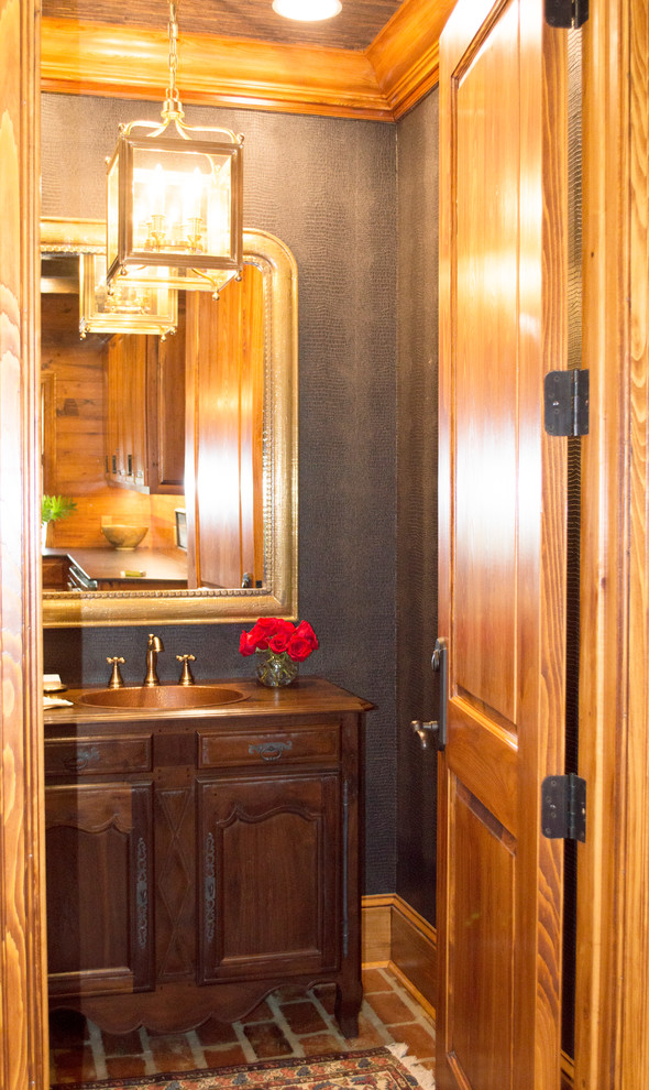 ニューオリンズにある中くらいなトラディショナルスタイルのおしゃれなトイレ・洗面所 (レイズドパネル扉のキャビネット、濃色木目調キャビネット、一体型トイレ	、グレーの壁、レンガの床、一体型シンク、銅の洗面台) の写真