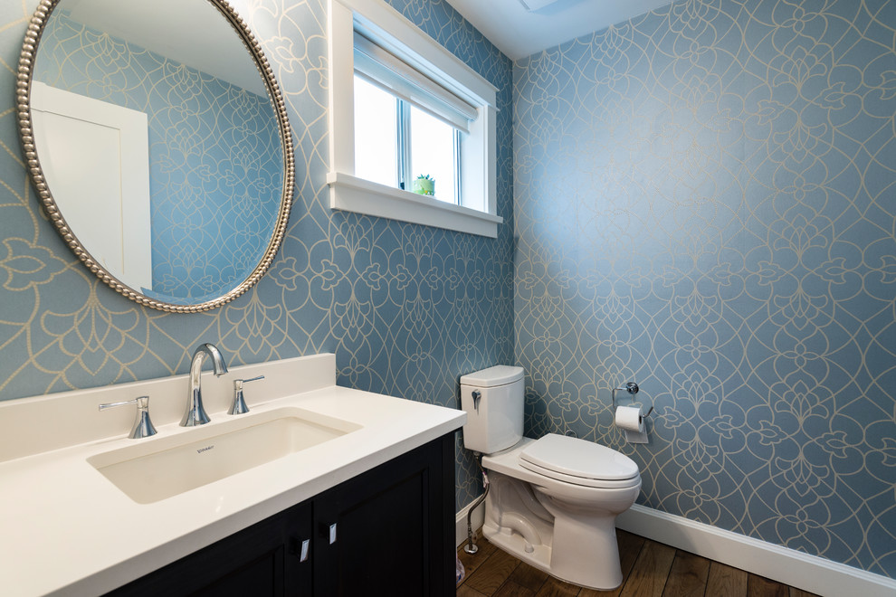 Cette image montre un WC et toilettes traditionnel en bois foncé de taille moyenne avec un placard à porte shaker, WC séparés, un mur bleu, parquet clair, un lavabo encastré et un plan de toilette en quartz modifié.