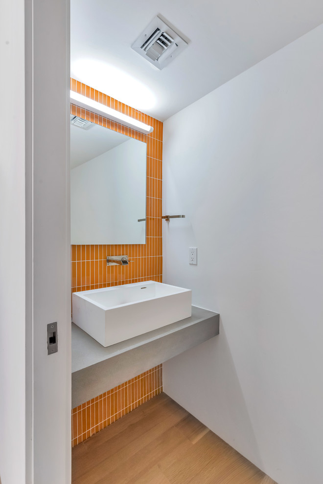 Foto de aseo actual con baldosas y/o azulejos naranja, paredes blancas, suelo de madera en tonos medios, lavabo sobreencimera, suelo marrón y encimeras grises