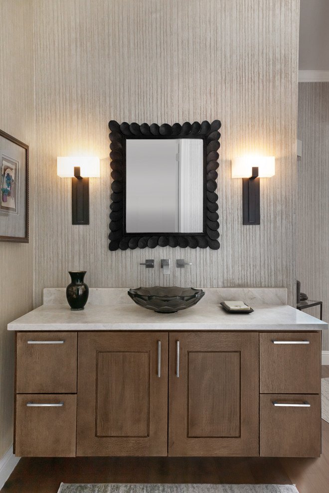 Example of a mid-sized transitional brown floor and medium tone wood floor powder room design in Austin with brown cabinets, multicolored walls, a vessel sink, white countertops, shaker cabinets and quartzite countertops