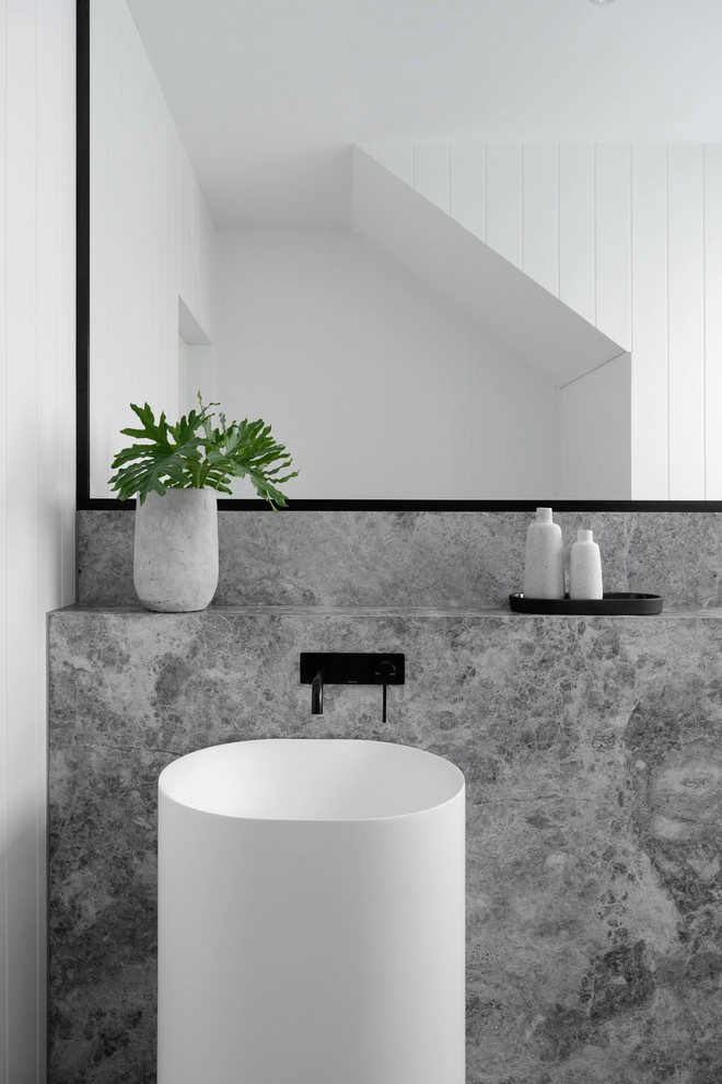 Bild på ett stort funkis grå grått toalett, med en toalettstol med hel cisternkåpa, vit kakel, vita väggar, klinkergolv i keramik, ett piedestal handfat, marmorbänkskiva och grått golv