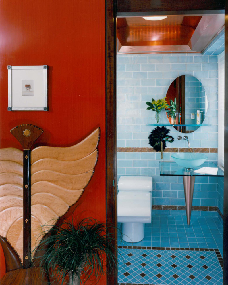 Idée de décoration pour un WC et toilettes design de taille moyenne avec WC à poser, un mur bleu, un sol en carrelage de céramique, une vasque, un plan de toilette en verre et un sol bleu.