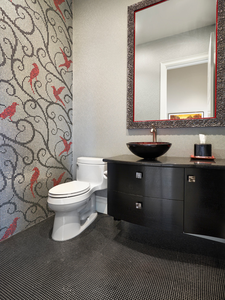 Inredning av ett modernt toalett, med möbel-liknande, svarta skåp, en toalettstol med hel cisternkåpa, flerfärgad kakel, mosaik, flerfärgade väggar, ett fristående handfat och svart golv