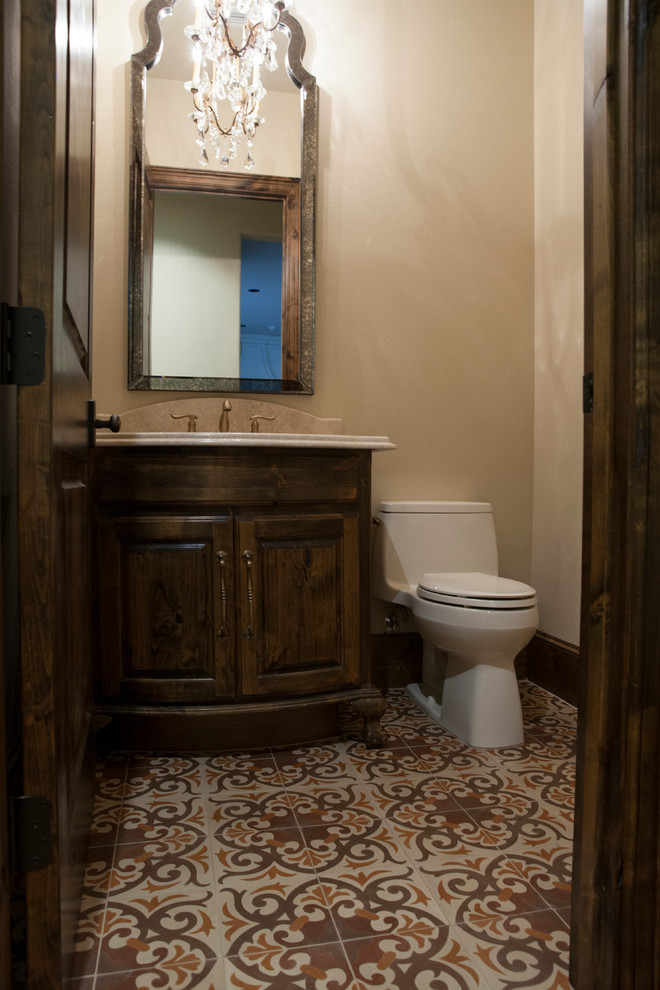 Exempel på ett litet medelhavsstil toalett, med luckor med upphöjd panel, skåp i mörkt trä, en toalettstol med hel cisternkåpa, flerfärgad kakel, beige väggar, ett nedsänkt handfat, granitbänkskiva och cementgolv
