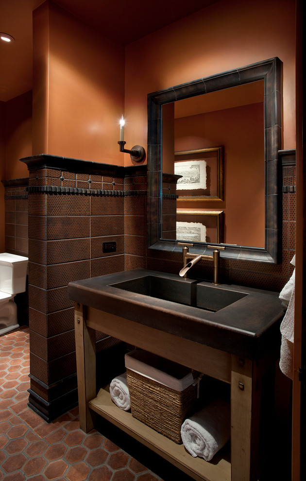 Kleine Mediterrane Gästetoilette mit integriertem Waschbecken, braunen Fliesen, oranger Wandfarbe, Terrakottaboden und schwarzer Waschtischplatte in Phoenix