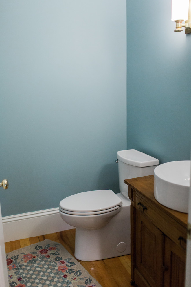Kleine Klassische Gästetoilette mit profilierten Schrankfronten, dunklen Holzschränken, Wandtoilette mit Spülkasten, blauer Wandfarbe, hellem Holzboden, Aufsatzwaschbecken, Travertin-Waschtisch und braunem Boden in Boston