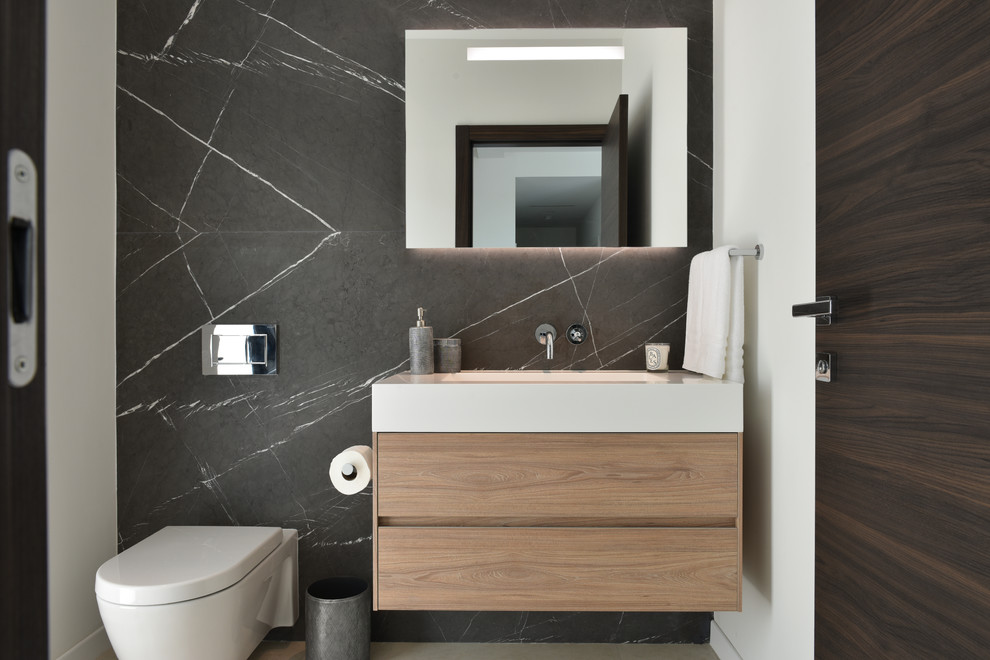 Inspiration for a contemporary cloakroom in Miami with flat-panel cabinets, light wood cabinets, a wall mounted toilet, marble tiles, black walls, an integrated sink and white worktops.