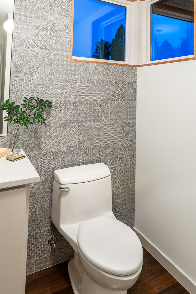 Exemple d'un WC et toilettes rétro de taille moyenne avec un placard à porte plane, des portes de placard blanches, WC à poser, un carrelage gris, des carreaux de béton, un mur multicolore, parquet foncé, un lavabo encastré, un plan de toilette en quartz modifié, un sol marron et un plan de toilette blanc.