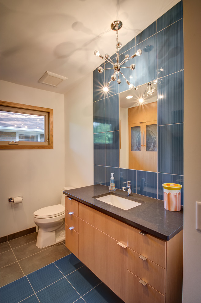 Cette image montre un WC et toilettes vintage en bois clair avec un lavabo encastré, un placard à porte plane, un plan de toilette en surface solide, un carrelage bleu, des carreaux de céramique, un mur blanc, un sol en carrelage de céramique et un sol multicolore.