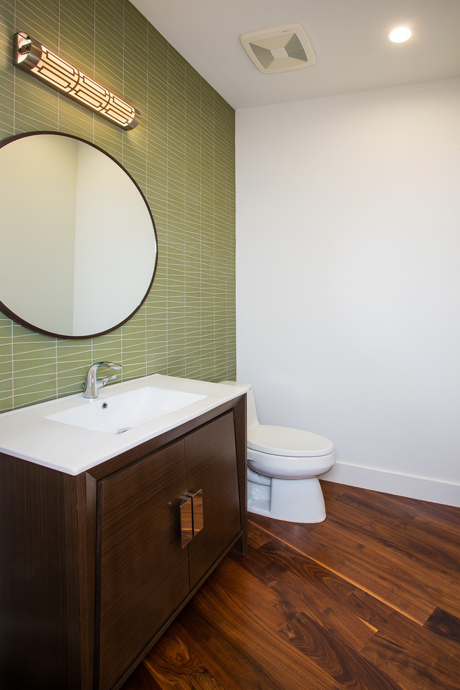 Photo of a small retro cloakroom in Dallas with flat-panel cabinets, dark wood cabinets, a one-piece toilet, green tiles, glass tiles, white walls, dark hardwood flooring, an integrated sink, engineered stone worktops and brown floors.
