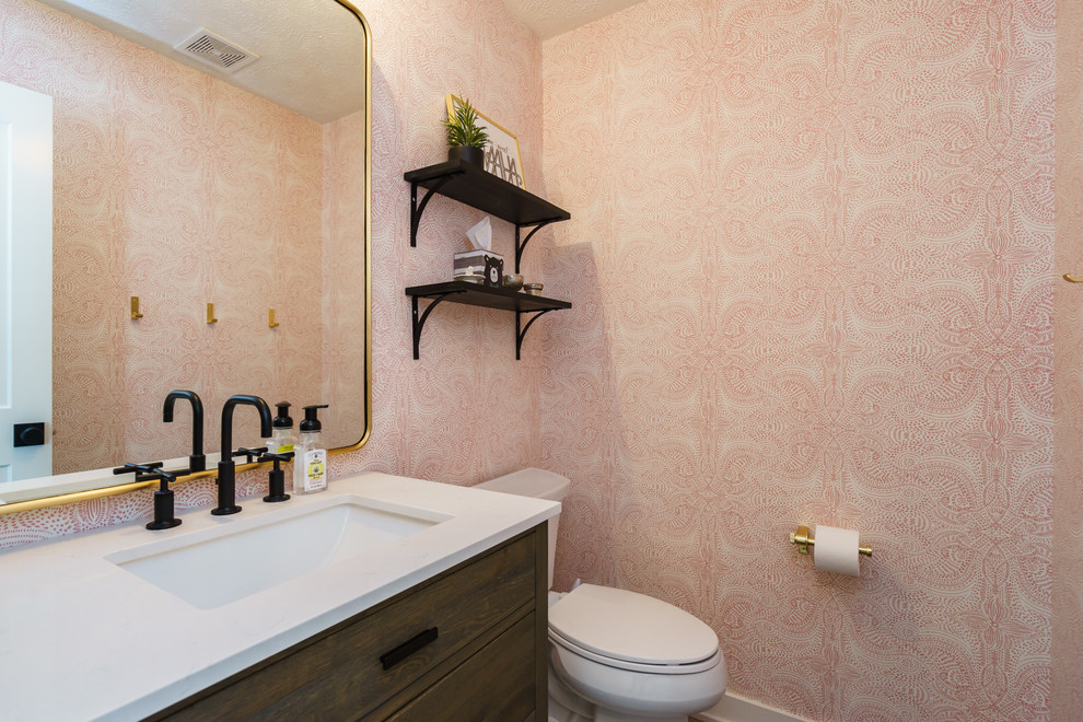 Kleine Moderne Gästetoilette mit flächenbündigen Schrankfronten, dunklen Holzschränken, Wandtoilette mit Spülkasten, rosa Wandfarbe, Mineralwerkstoff-Waschtisch und weißer Waschtischplatte in Omaha