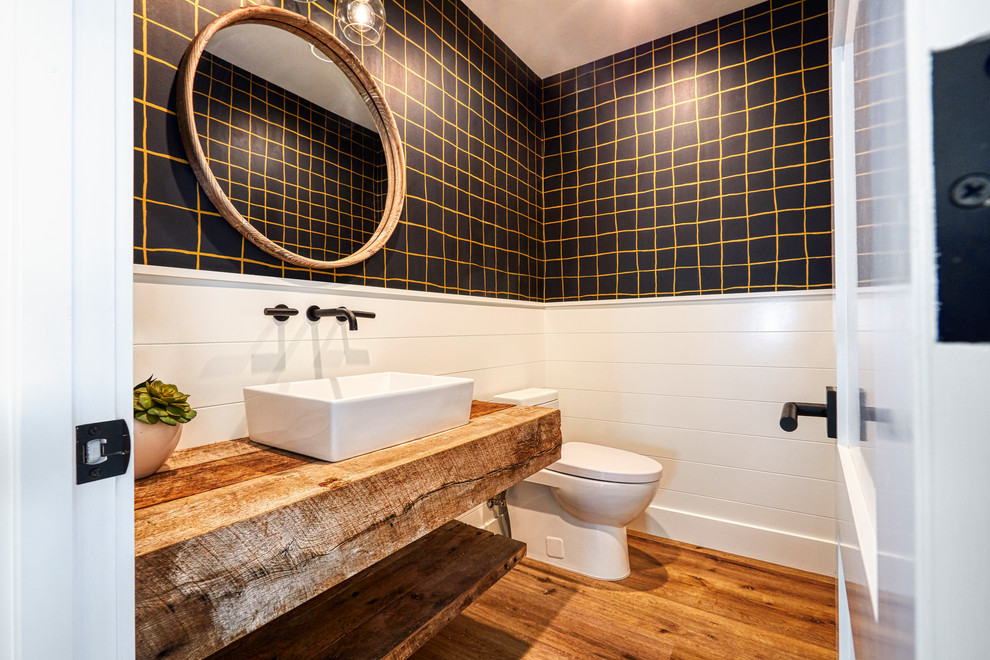 Example of a cottage vinyl floor powder room design in Orange County with furniture-like cabinets, medium tone wood cabinets, a one-piece toilet, black walls, a vessel sink, wood countertops and brown countertops
