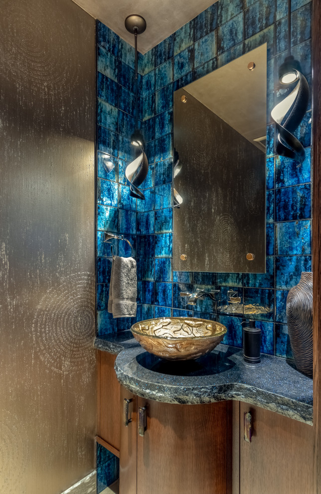 Kleine Moderne Gästetoilette mit flächenbündigen Schrankfronten, hellbraunen Holzschränken, blauen Fliesen, Fliesen aus Glasscheiben, Porzellan-Bodenfliesen, Aufsatzwaschbecken, Granit-Waschbecken/Waschtisch und schwarzer Waschtischplatte in Omaha