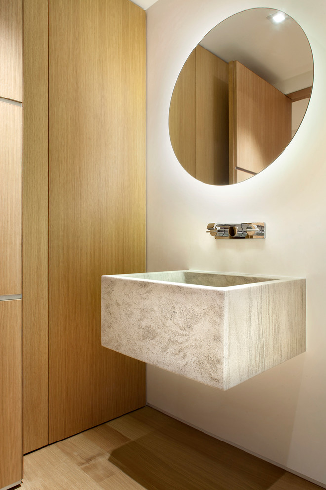 Modelo de aseo contemporáneo con paredes blancas, suelo de madera clara, lavabo suspendido y suelo beige