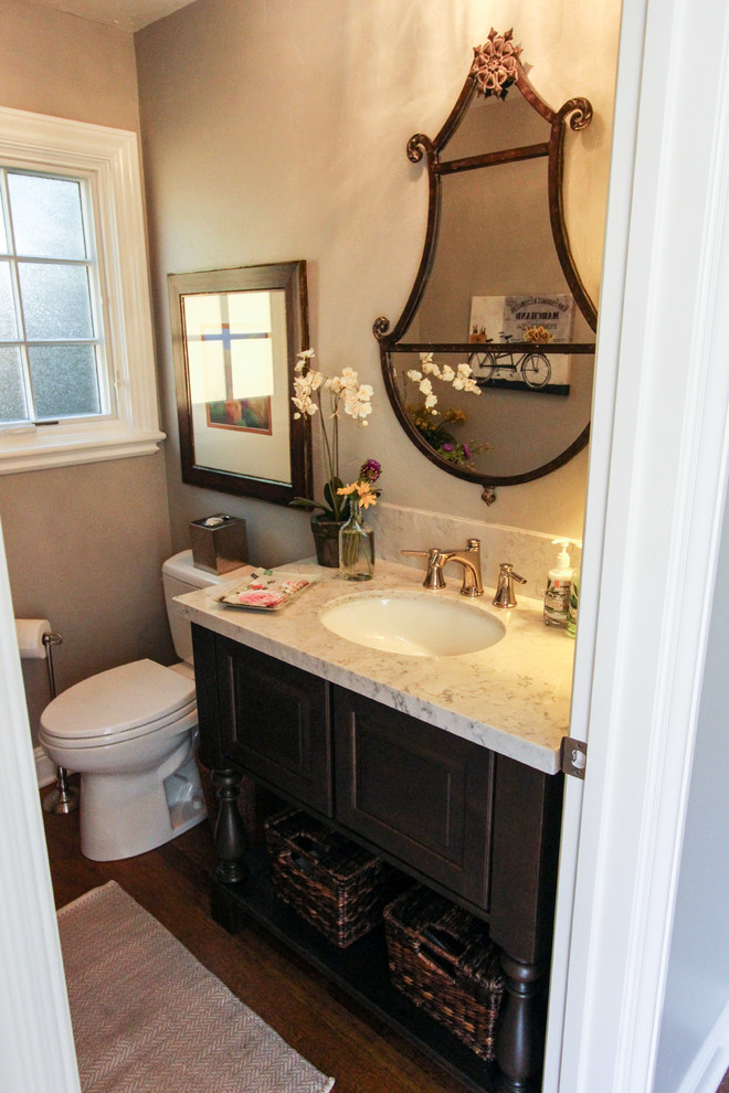 Small elegant white tile and stone slab medium tone wood floor powder room photo in San Francisco with raised-panel cabinets, dark wood cabinets, a two-piece toilet, beige walls, an undermount sink and quartz countertops