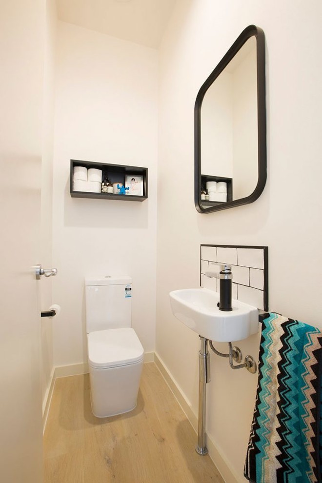 Small modern cloakroom in Melbourne with a one-piece toilet, white tiles, metro tiles, white walls, light hardwood flooring, a wall-mounted sink and beige floors.