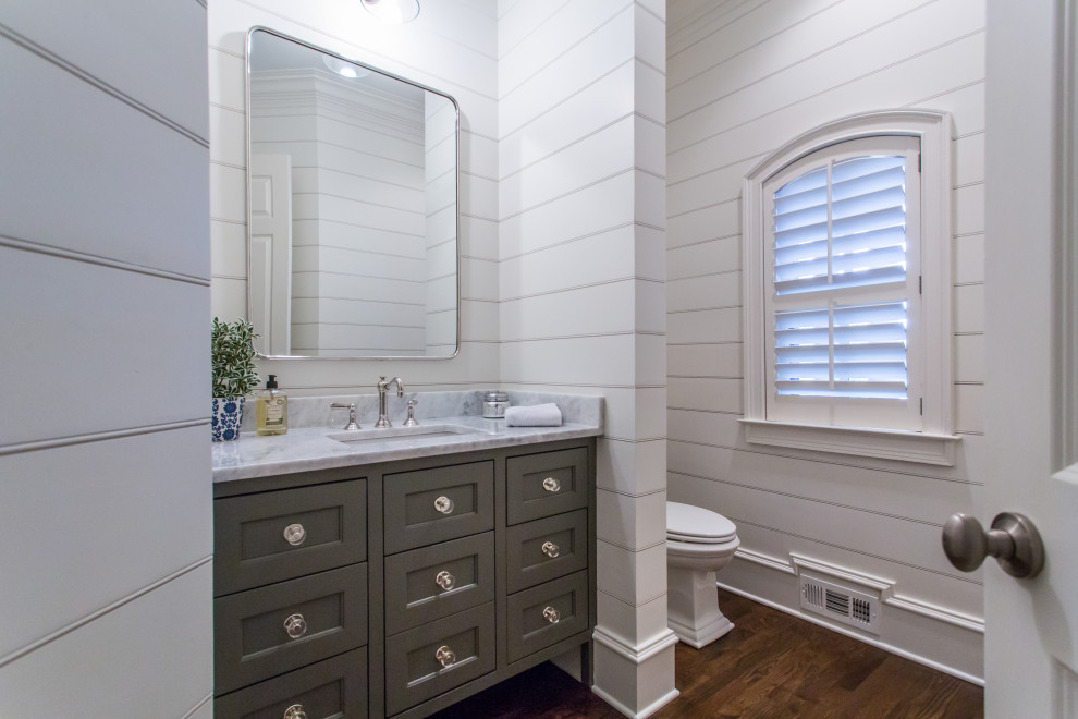 Landhaus Gästetoilette mit Kassettenfronten, grauen Schränken, weißer Wandfarbe, dunklem Holzboden und weißer Waschtischplatte in Atlanta