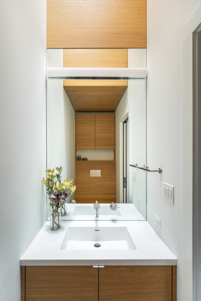 Cette photo montre un petit WC suspendu moderne avec un placard à porte plane, des portes de placard blanches, un mur blanc, un lavabo intégré, un plan de toilette en surface solide, un plan de toilette blanc, meuble-lavabo encastré et un plafond en bois.