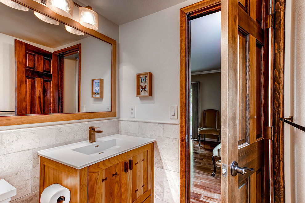 Exempel på ett litet amerikanskt toalett, med ett integrerad handfat, skåp i shakerstil, skåp i mellenmörkt trä, bänkskiva i akrylsten, en toalettstol med separat cisternkåpa, beige kakel, keramikplattor och beige väggar