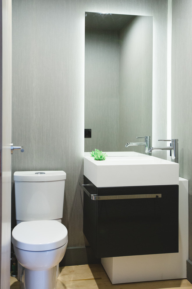 Große Moderne Gästetoilette mit integriertem Waschbecken, flächenbündigen Schrankfronten, schwarzen Schränken, Toilette mit Aufsatzspülkasten, grauer Wandfarbe und hellem Holzboden in Calgary