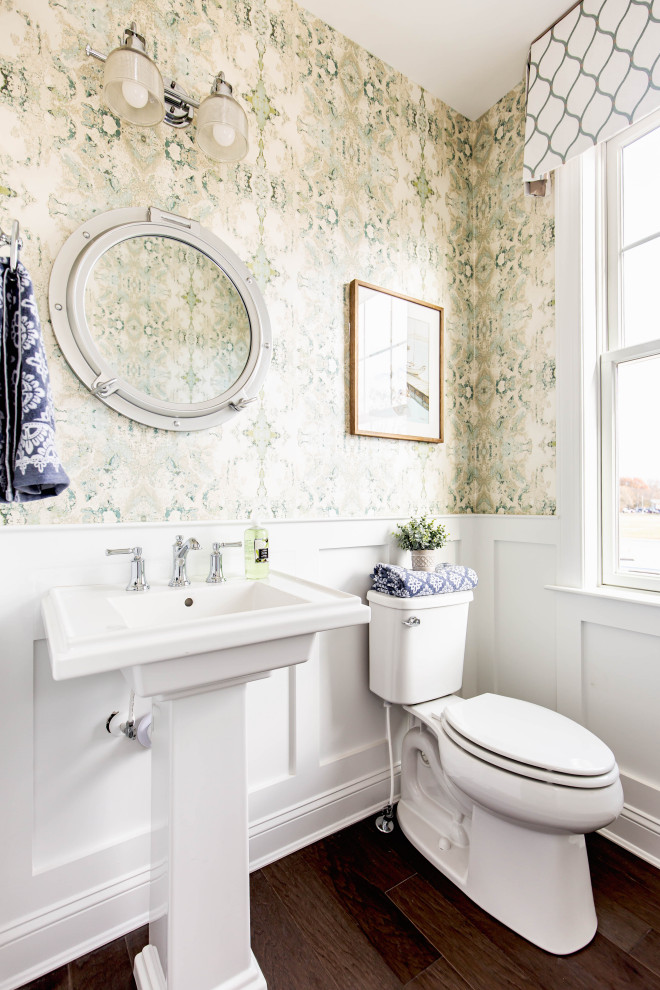 Immagine di un bagno di servizio tradizionale con WC a due pezzi, pareti verdi, parquet scuro, lavabo a colonna, pavimento marrone e boiserie