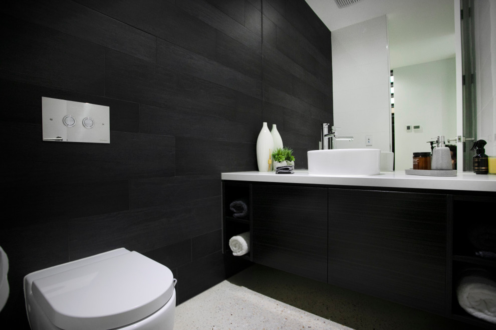Große Moderne Gästetoilette mit flächenbündigen Schrankfronten, schwarzen Schränken, schwarzen Fliesen, schwarzer Wandfarbe, Betonboden, Granit-Waschbecken/Waschtisch, weißer Waschtischplatte, schwebendem Waschtisch und Tapetenwänden in Melbourne
