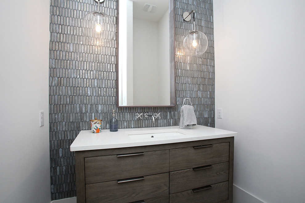 Powder room - mid-sized modern gray tile and glass tile ceramic tile and gray floor powder room idea in Dallas with furniture-like cabinets, gray cabinets, a wall-mount toilet, white walls, an undermount sink and solid surface countertops
