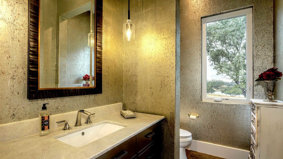 Mittelgroße Landhaus Gästetoilette mit verzierten Schränken, Toilette mit Aufsatzspülkasten, beiger Wandfarbe, Marmor-Waschbecken/Waschtisch, grauer Waschtischplatte, dunklen Holzschränken, dunklem Holzboden, Unterbauwaschbecken und braunem Boden in Houston