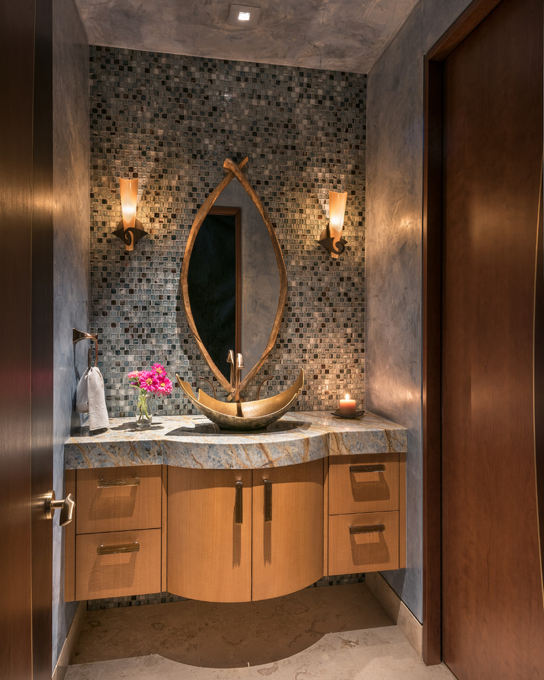 Cette image montre un grand WC et toilettes design en bois clair avec un placard à porte plane, un sol en calcaire, une vasque, un plan de toilette en granite, un carrelage gris, un mur gris, mosaïque et un sol beige.