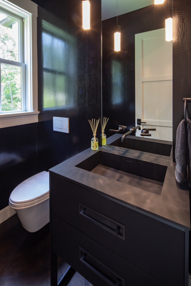 Example of a large cottage dark wood floor and black floor powder room design in Boston with flat-panel cabinets, black cabinets, a wall-mount toilet, black walls, an integrated sink, solid surface countertops and black countertops