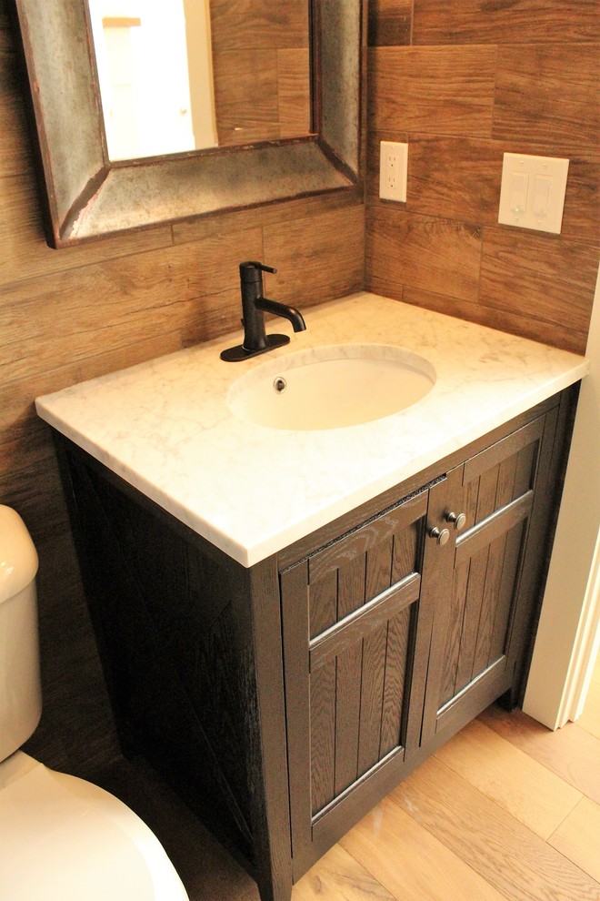 Medium sized country cloakroom in Seattle with shaker cabinets, black cabinets, a two-piece toilet, brown tiles, ceramic tiles, blue walls, medium hardwood flooring, a submerged sink, marble worktops, brown floors and white worktops.