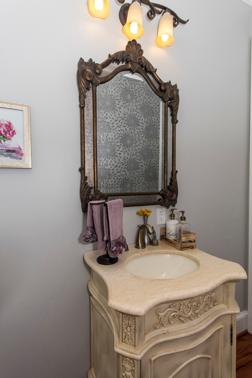 Example of a large classic medium tone wood floor powder room design in Baltimore with furniture-like cabinets, distressed cabinets, a two-piece toilet, gray walls, an integrated sink and marble countertops