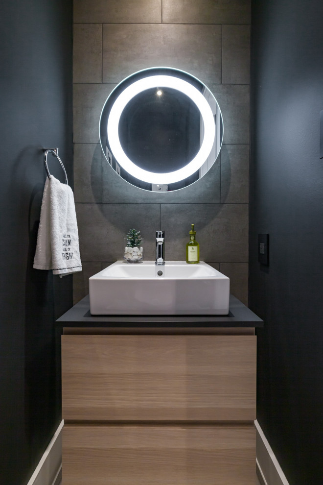 Пример оригинального дизайна: маленький туалет в стиле модернизм с плоскими фасадами, светлыми деревянными фасадами, унитазом-моноблоком, серой плиткой, керамогранитной плиткой, черными стенами, полом из керамогранита, настольной раковиной, столешницей из ламината, серым полом и черной столешницей для на участке и в саду