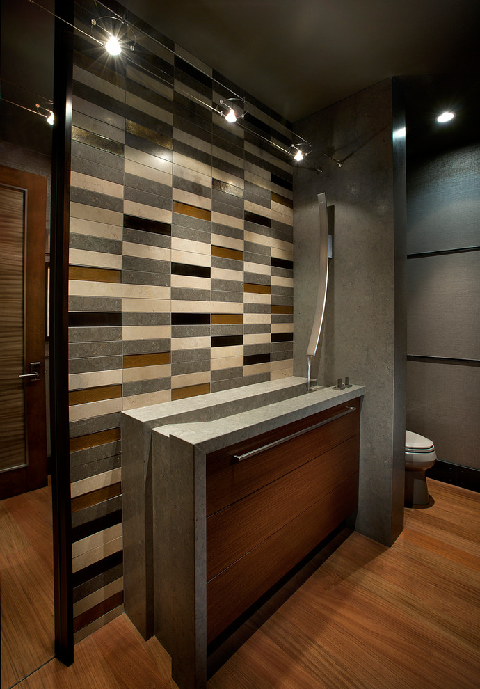 Пример оригинального дизайна: туалет в современном стиле с монолитной раковиной, плоскими фасадами, темными деревянными фасадами, разноцветной плиткой, плиткой из известняка, серыми стенами, паркетным полом среднего тона, коричневым полом и серой столешницей