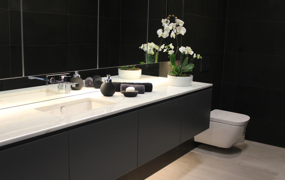 Modern inredning av ett mellanstort toalett, med släta luckor, en vägghängd toalettstol, grå väggar, kalkstensgolv, ett undermonterad handfat, svarta skåp och svart kakel