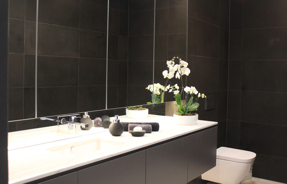 Exemple d'un WC suspendu moderne de taille moyenne avec un placard à porte plane, des portes de placard grises, un carrelage gris, un carrelage de pierre, un mur gris et un lavabo encastré.