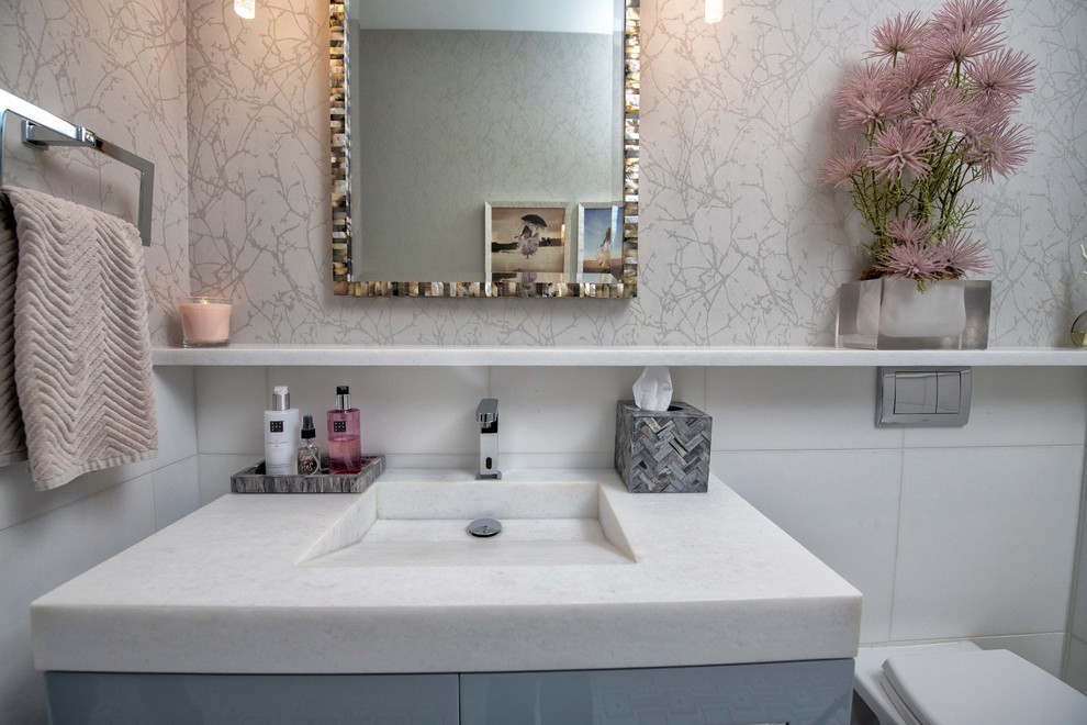 Inspiration for a mid-sized transitional white tile and marble tile mosaic tile floor and multicolored floor powder room remodel in New York with flat-panel cabinets, gray cabinets, a wall-mount toilet, gray walls, an integrated sink, marble countertops and white countertops