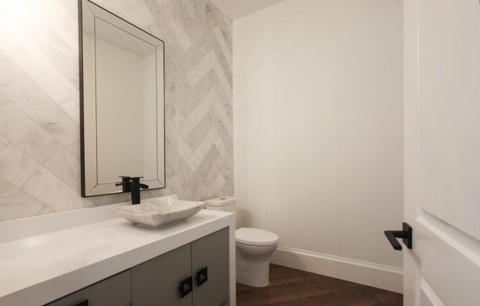 Foto på ett litet funkis toalett, med släta luckor, grå skåp, en toalettstol med hel cisternkåpa, vit kakel, vita väggar, ett fristående handfat och bänkskiva i akrylsten