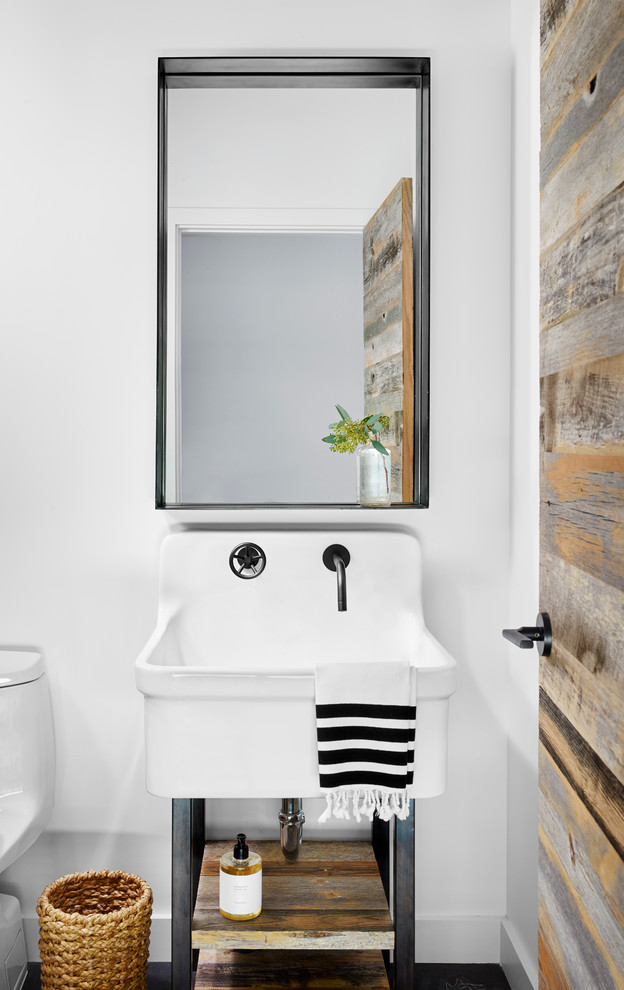 Inredning av ett industriellt vit vitt toalett, med vita väggar, ett konsol handfat, mörkt trägolv och svart golv